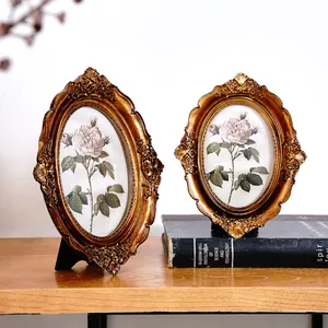 Pair of ornate vintage bronze resin oval photo frames with rose prints on wooden shelf