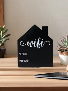 A decorative black house-shaped WiFi password sign placed on a wooden desk with plants