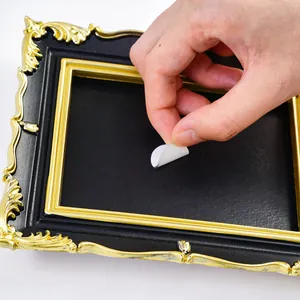 Close-up showing a hand peeling a white adhesive sticker on black DIY vintage picture frame
