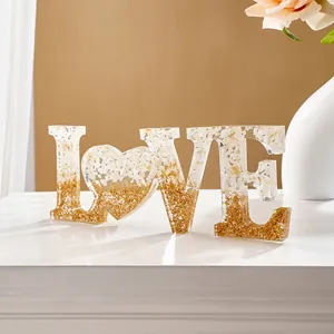 Macrodetail van LOVE harsornament met witte schelpen en goudkleurig glitterverloop decor.