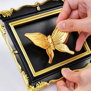 Hand placing gold butterfly into vintage black and gold frame for DIY wall decor