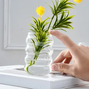 Detailaufnahme einer transparenten Raupen-Glasvase mit Grünpflanzen für die Dekoration.