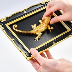 Close-up of golden lizard figurine being placed into vintage black and gold frame