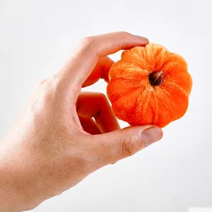 Close-up of small orange plush pumpkin held in hand showing soft velvet texture