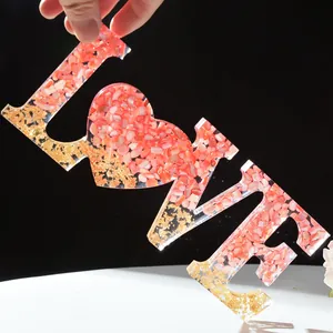 Detail van resin LOVE-bord met roze stenen en gouden vlokken voor bruiloft decoratie.