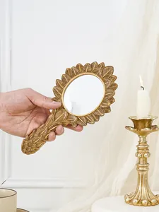 Vintage French gold leaf resin hand mirror held by hand against an elegant white background