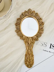Detailed view of vintage gold oval hand mirror with intricate resin leaf pattern frame.