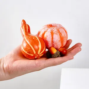 Primo piano di una mano con piccole zucche artificiali e ghiande per decorazioni fai da te autunnali