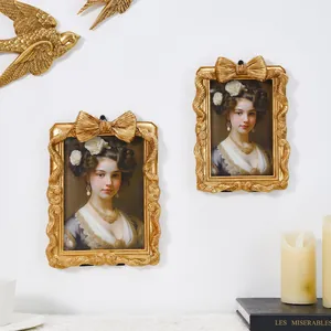 Detail von goldenen europäischen Vintage-Fotorahmen mit Schleifenmuster an einer weißen Wand.
