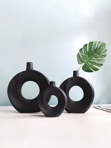 Detailansicht von drei mattschwarzen ringförmigen Vasen aus Harz mit einem Blatt.