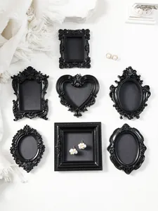 Seven vintage black miniature photo frames in diverse ornate shapes on white surface