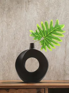 Moderne minimalistische schwarze Donut-Harzvase mit grünem Blatt auf einer Holzoberfläche