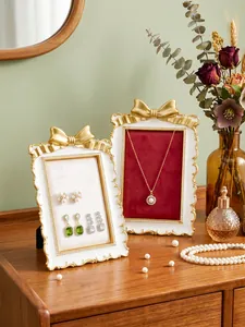 Gilded bow jewelry frames with velvet lining displayed on a wooden vanity table.