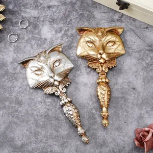 Close-up of vintage-style gold and silver fox-shaped resin hand mirrors on a grey texture.