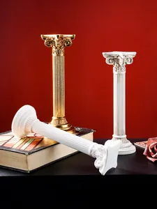 Detalle de candelabros de columna romana de resina blanca y dorada sobre libro antiguo.
