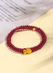 Dettaglio macro del bracciale a tre giri in granato da 4mm con ciondolo Pixiu d'oro