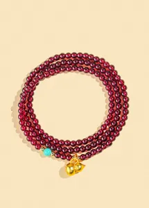 Dettaglio del bracciale con perline di granato, ciondolo hulu dorato e turchese