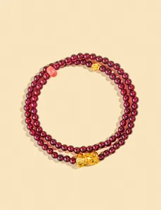 Dettaglio di perline di granato da 4 mm su un bracciale a triplo giro con ciondolo Pixiu dorato.