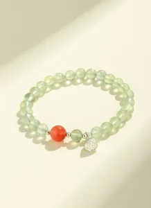 Detailed macro view of prehnite beaded bracelet with red agate and silver lotus charm.