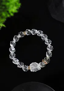 Detalle macro de una pulsera de cristal blanco facetado con dijes de zorro y corona