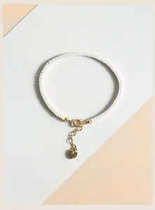 Macro detail view of a minimalist white stone beaded bracelet featuring a gold heart charm