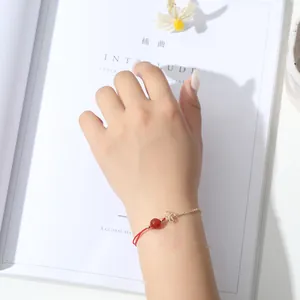 Detail eines minimalistischen Armbands mit roter Kordel, Goldkette und zartem Blumenanhänger