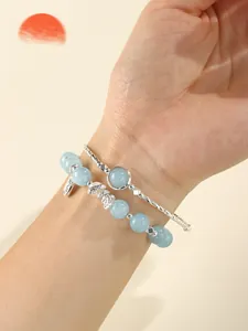 Close-up view of aquamarine beaded bracelet and silver bangle on a woman's wrist