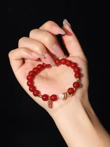 Macro detail of red agate beaded bracelet featuring pearl and gold blessing charm