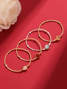 Top view of gold and silver twisted bracelets with colorful round gemstones on red