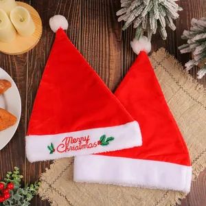 Two velvet plush red Santa hats with Merry Christmas embroidery on festive wooden table