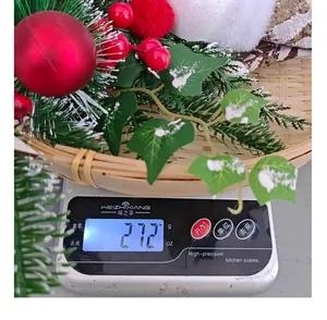 Close-up of a Christmas wreath with red baubles on a digital scale weighing 27.2g.