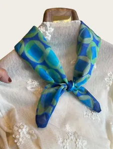 Detail view of a blue and green geometric print silk scarf knotted on a white top