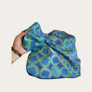 Detailed texture of a geometric blue and green printed lightweight silk scarf.