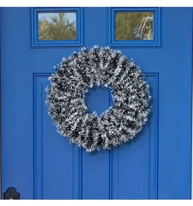 Detail of a fluffy black and white Christmas tinsel wreath on a vibrant blue door