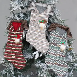 Three festive knitted Christmas stockings with gnome decorations on a snowy pine tree.