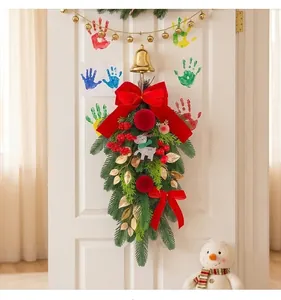 Detailed view of a Christmas teardrop swag with a red velvet bow and gold bell on a door.