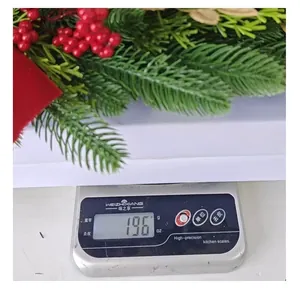 Detailed view of a green Christmas wreath with red berries being weighed on a scale