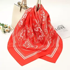 Close-up detail of a red satin square scarf featuring intricate white paisley patterns.