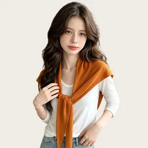Detailansicht eines weichen orangefarbenen Strick-Dreieckstuchs, elegant über einem weißen Oberteil.