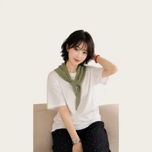 Detail of green knitted hollow triangular shawl styled as a shoulder cape over a white tee.