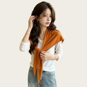 Model trägt ein orangefarbenes, leichtes, gestricktes Dreieckstuch über einem weißen Oberteil