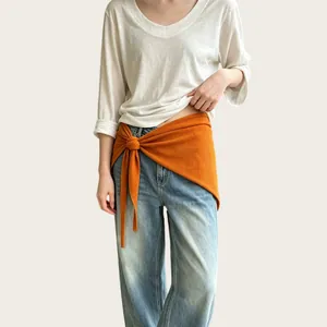 Detail eines orangefarbenen Strick-Dreieckstuchs, das als Accessoire um die Taille gebunden ist