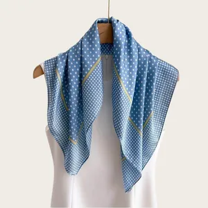 Elegante foulard in seta a pois blu e bianchi esposto su una gruccia di legno chiaro.