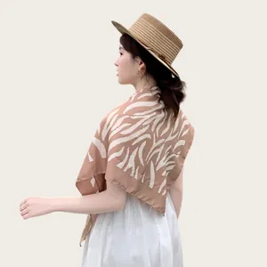 Dettaglio di un elegante scialle in seta zebrata su una modella con cappello di paglia.