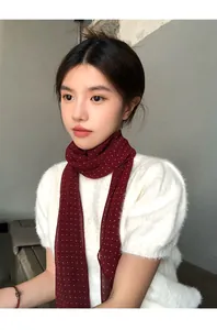 Dettaglio di una sciarpa sottile bordeaux a pois indossata con un maglione bianco.