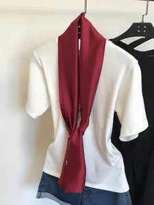 Détail d'un foulard en soie étroit marron noué sur un t-shirt blanc sur un cintre