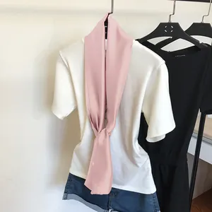 Détail d'un foulard en soie rose étroit porté avec un T-shirt blanc et un short.