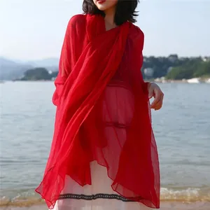 Detailed view of model wearing a vibrant red oversized summer sunscreen shawl at the beach