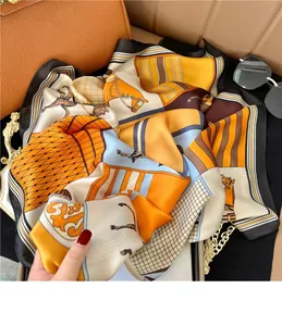 Detail eines eleganten quadratischen Seidenschals mit Reitmotiven in Orange und Blau.