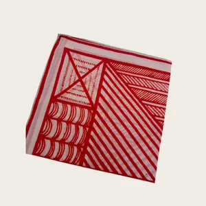 Close-up of a folded silk scarf featuring bold red geometric patterns on white fabric.